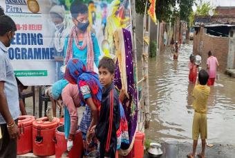 As team members prepare themselves to serve food, localites carry their utensils to serve their families