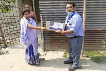 Akshaya Patra employees hand over grocery kits to a woman in need.